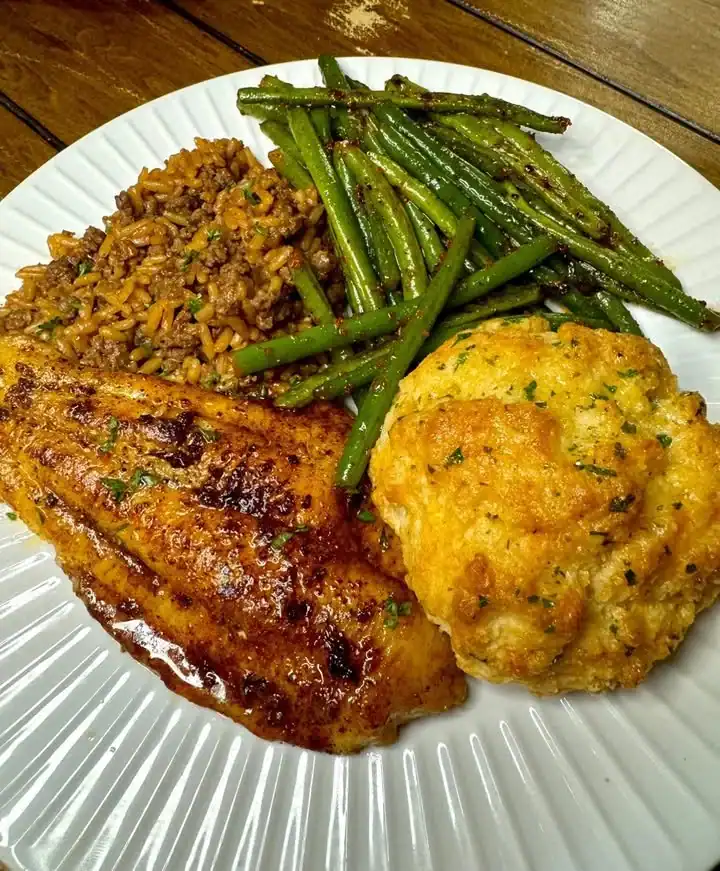 Plate of grilled catfish with dirty rice, cheddar bay biscuits, and green beans.