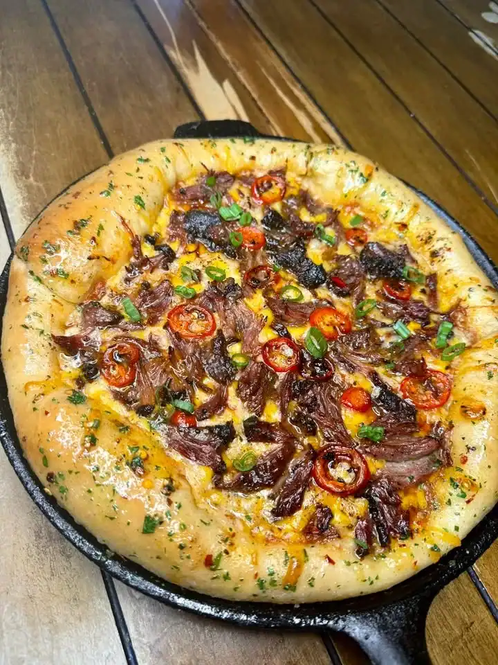 Smoked Sweet Chili Jerk Oxtail Pizza topped with fresh herbs and vibrant ingredients