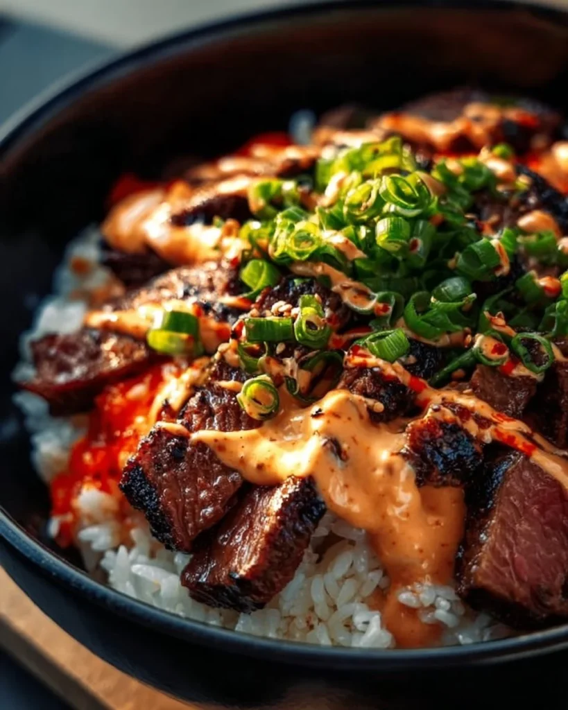 Bowl of Korean BBQ steak served over rice with colorful vegetables and sauce.