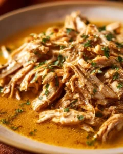 Creamy shredded chicken dish served on a plate with herbs and spices.